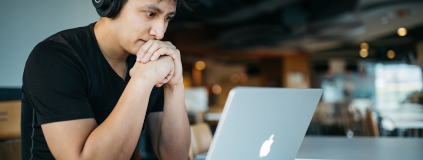 man wearing headphones while sitting on chair in front of MacBook