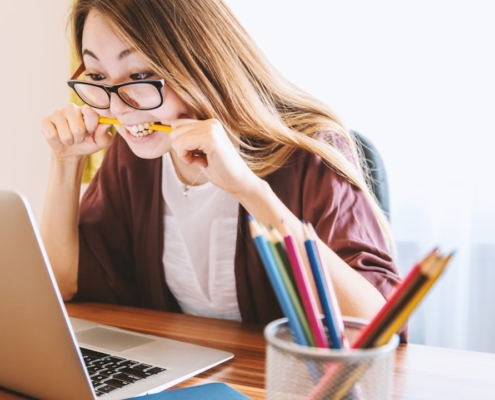 woman biting pencil while sitting on chair in front of computer during daytime